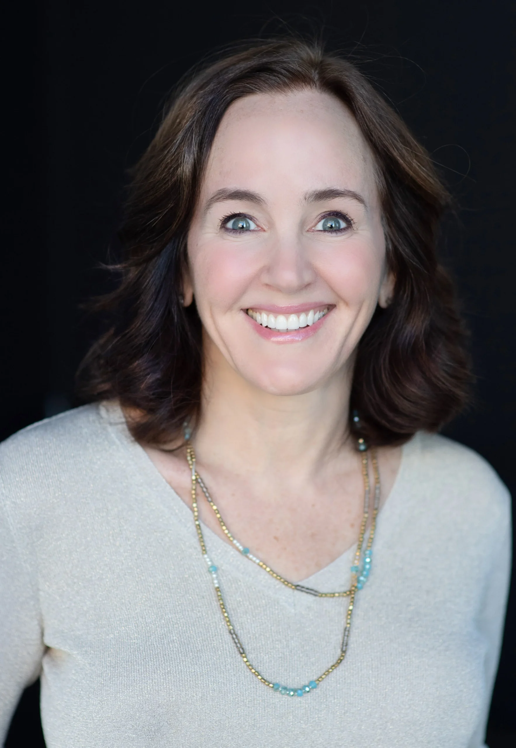 Author Dana Suskind, MD. She is white with long brown hair. She is wearing a white blouse with a beaded necklace.